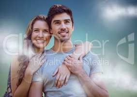 Woman with arms around man against blue green background with clouds
