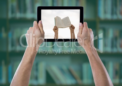 Hand with tablet showing hands with book against blurry bookshelf with green overlay