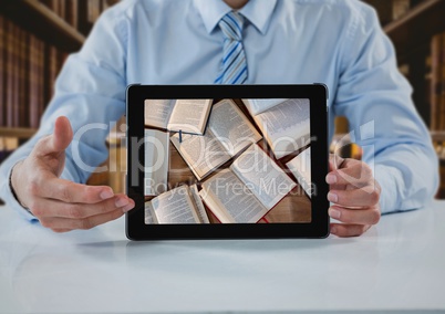Business man at table with tablet showing open books against blurry bookshelves