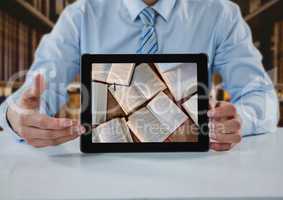 Business man at table with tablet showing open books against blurry bookshelves