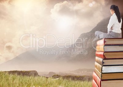 Woman sitting on Books stacked by mountain sky