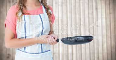 Woman in apron with frying pan against blurry wood panel