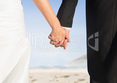 Bride and groom lower bodies holding hands against blurry beach
