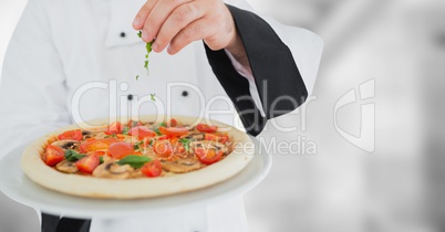 Chef putting herbs on pizza against blurry grey background