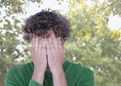 Upset stressed man hiding in hands under trees