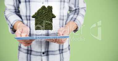 Man mid section with tablet and leaf house against green background