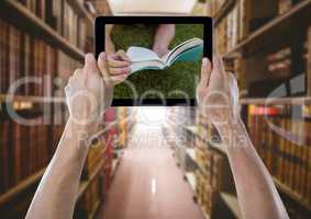 Hands with tablet showing book against grass against bookshelves
