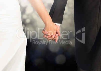 Wedding couple holding hands against glowing lights