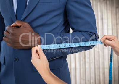 Man in suit mid section being measured against blurry wood panel