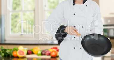 Chef with wok against blurry kitchen with vegetables