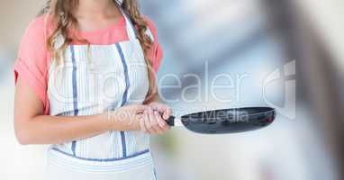 Woman in apron with frying pan against blurry window