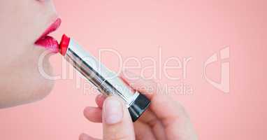 Close up of woman putting on lipstick against pink background