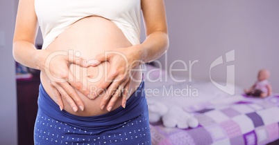 Pregnant woman mid section making heart shape in blurry bedroom with pink overlay