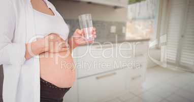 Pregnant woman mid section with glass of water in blurry kitchen