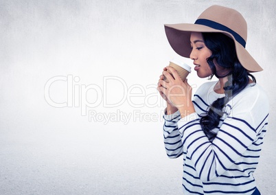 Woman with hat drinking from coffee cup against white wall