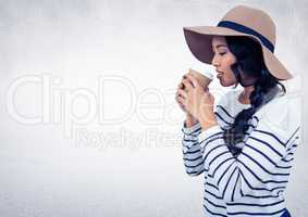 Woman with hat drinking from coffee cup against white wall