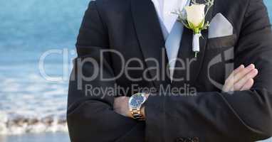 Groom mid section with arms folded against blurry beach shore