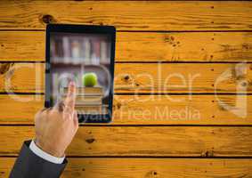Hand touching tablet showing book pile with apple on yellow table
