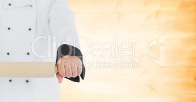 Chef with rolling pin against blurry yellow wood panel