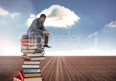 Businessman sitting on Books stacked by blue cloudy sky