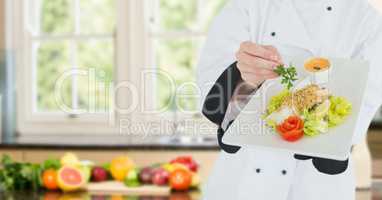Chef with plate of food against blurry kitchen with vegetables