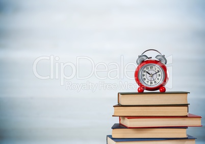 Pile of books and clock against blurry grey wood panel