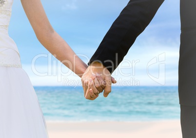 Bride and groom holding hands at blurry beach