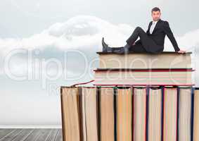 Man sitting on Books stacked by cloudy sky