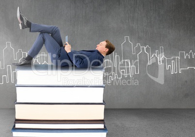 Businessman lying on Books stacked by city drawing with tablet