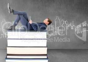 Businessman lying on Books stacked by city drawing with tablet