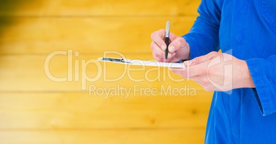 Mechanic with clipboard against blurry yellow wood panel