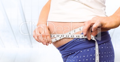 Pregnant woman mid section with measuring tape against blurry window