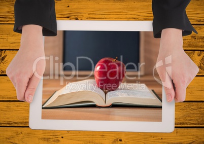 Hands with tablet on yellow table showing book with red apple