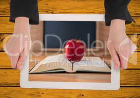 Hands with tablet on yellow table showing book with red apple