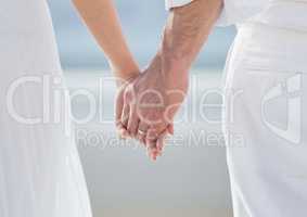 Bride and groom lower bodies holding hands against blurry beach