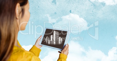 Woman with tablet showing white buildings against sky with clouds