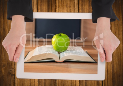 Hands with tablet on table showing book with green apple