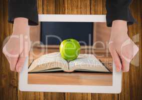 Hands with tablet on table showing book with green apple