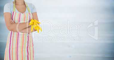 Woman in apron with arms folded and gloves off against blurry grey wood panel