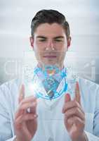 Man in lab coat holding up glass device with blue medical interface and flare against grey backgroun