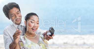 Man proposing to woman against blurry beach
