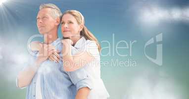 Woman with arms around man against blue green background with clouds and flare