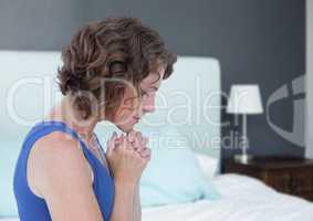 Woman praying hopeful and sad next to bed