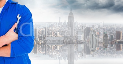 Mechanic with arms folded and wrench against blurry skyline