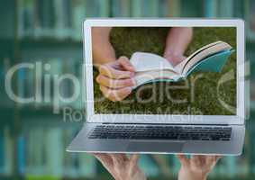 Hands with laptop showing book on grass against blurry bookshelf with green overlay