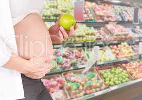 Pregnant woman mid section holding apple in blurry vegetable aisle