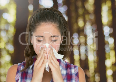 Young woman with hayfever blowing nose in forest trees