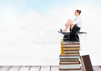 woman sitting on Books stacked by blue sky with graduation hat