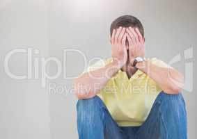 Upset man sitting down with face in hands against grey background