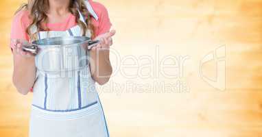 Woman in apron with pan against blurry yellow wood panel